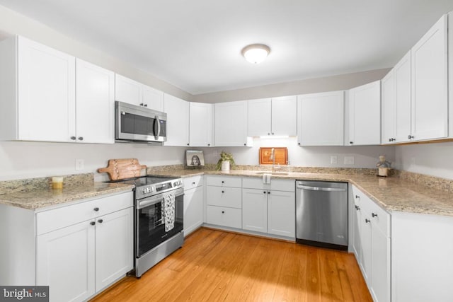 kitchen with stainless steel appliances, white cabinetry, light stone counters, and light wood-style floors
