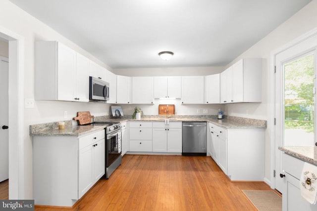 kitchen featuring stainless steel appliances, white cabinets, light stone countertops, light wood-style floors, and a sink
