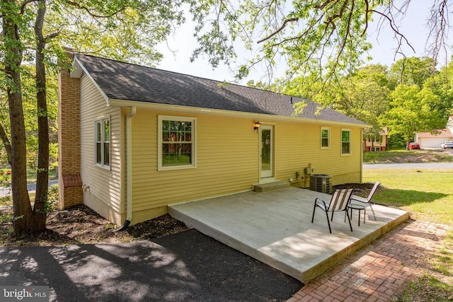 back of house featuring a chimney, a patio, roof with shingles, and central air condition unit