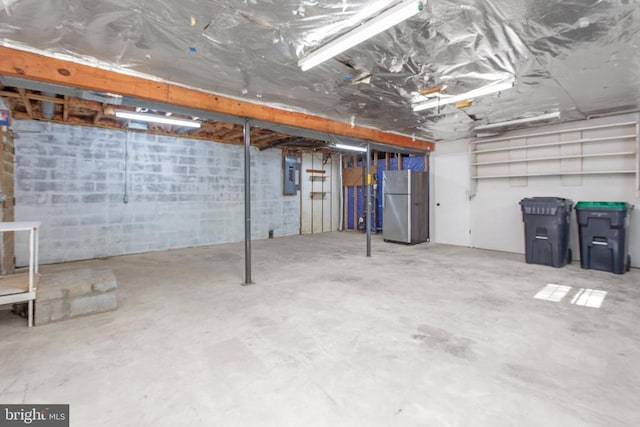unfinished basement with freestanding refrigerator and electric panel