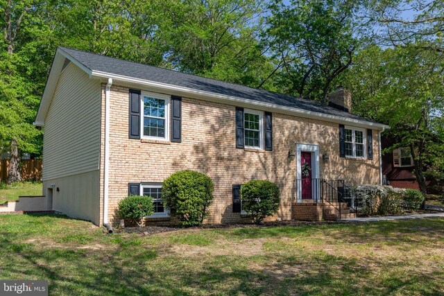 raised ranch with a chimney, a front lawn, and brick siding