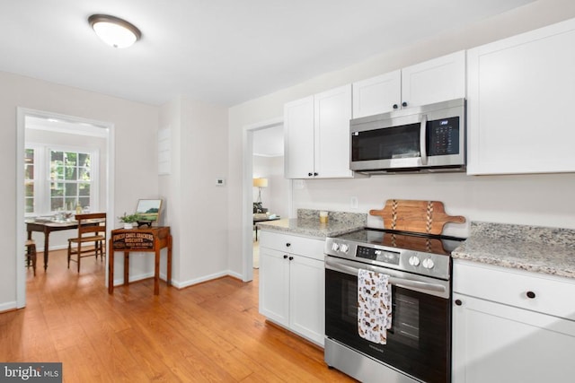 kitchen with appliances with stainless steel finishes, white cabinets, light wood-style floors, baseboards, and light stone counters