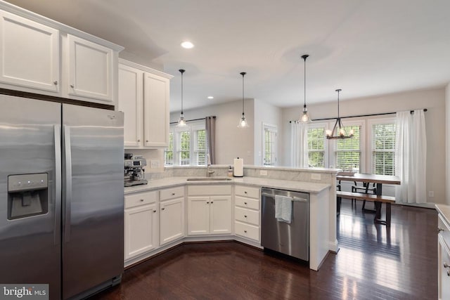 kitchen with appliances with stainless steel finishes, a sink, dark wood-type flooring, a peninsula, and white cabinets