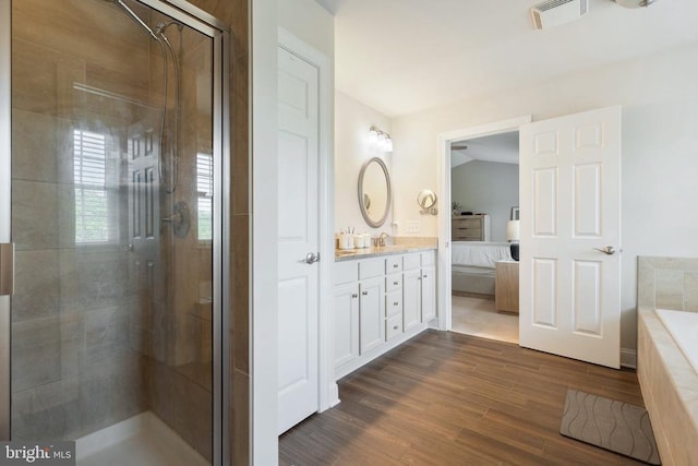 ensuite bathroom featuring a shower stall, double vanity, wood finished floors, and a tub to relax in