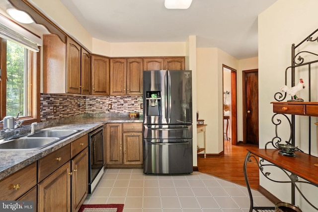 kitchen with refrigerator with ice dispenser, a sink, dishwasher, dark countertops, and brown cabinets