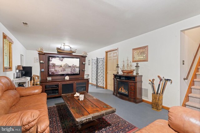 living room featuring a glass covered fireplace, stairway, and baseboards