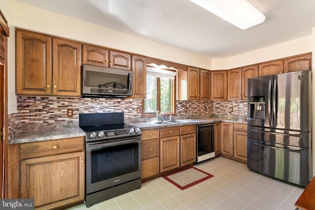 kitchen with appliances with stainless steel finishes, a sink, brown cabinetry, decorative backsplash, and dark countertops
