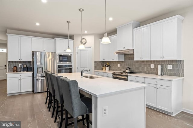 11326 Oakville Ln, Spotsylvania, VA 22551 - kitchen with appliances with stainless steel finishes, under cabinet range hood, tasteful backsplash, a breakfast bar area, and light wood-style flooring