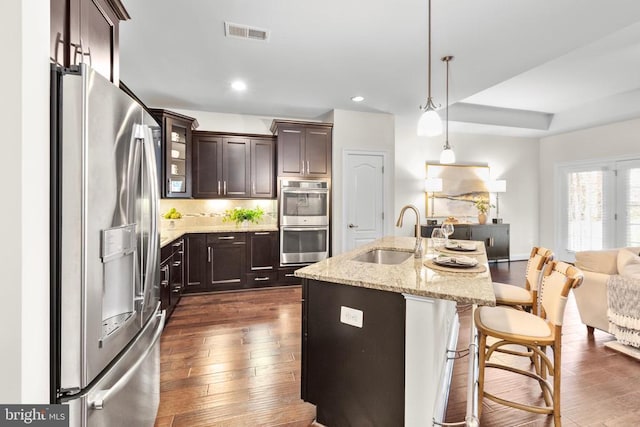 kitchen with dark brown cabinetry, stainless steel appliances, dark wood-type flooring, a sink, and visible vents