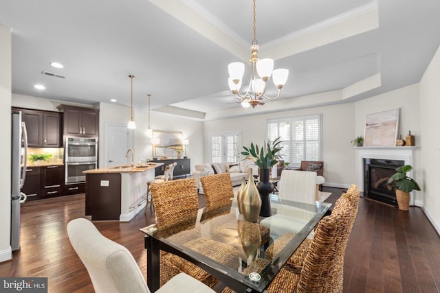 dining room with dark wood-style floors, a tray ceiling, a glass covered fireplace, and visible vents