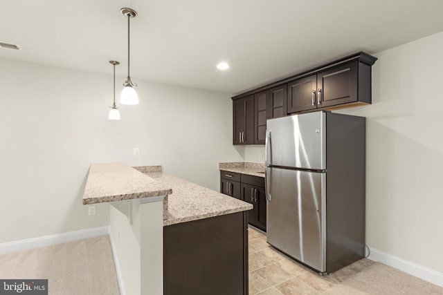 kitchen featuring a peninsula, baseboards, a kitchen breakfast bar, dark brown cabinets, and freestanding refrigerator