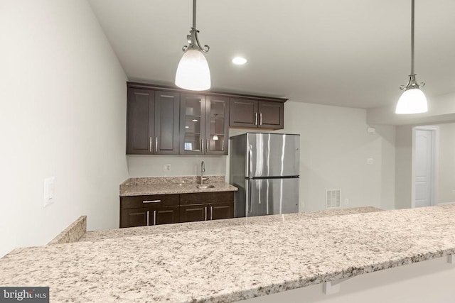 kitchen featuring dark brown cabinetry, visible vents, glass insert cabinets, freestanding refrigerator, and pendant lighting