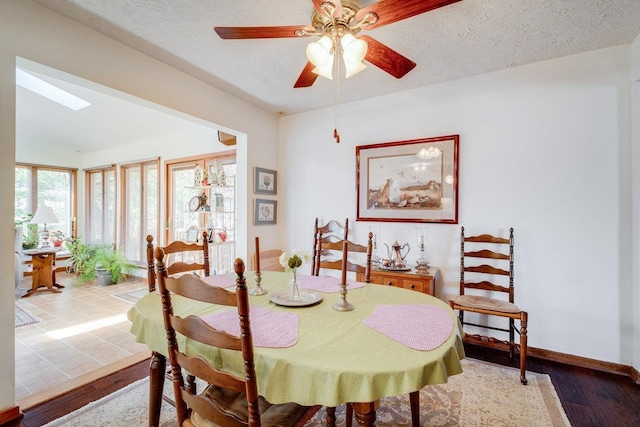 dining space featuring wood finished floors, a skylight, a textured ceiling, baseboards, and ceiling fan