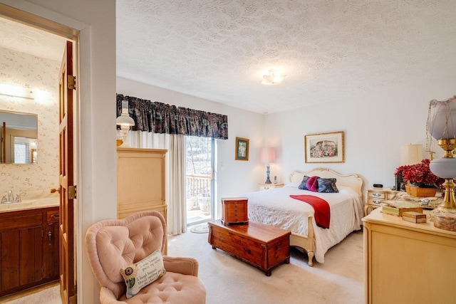 bedroom featuring a textured ceiling, ensuite bath, a sink, light carpet, and access to exterior