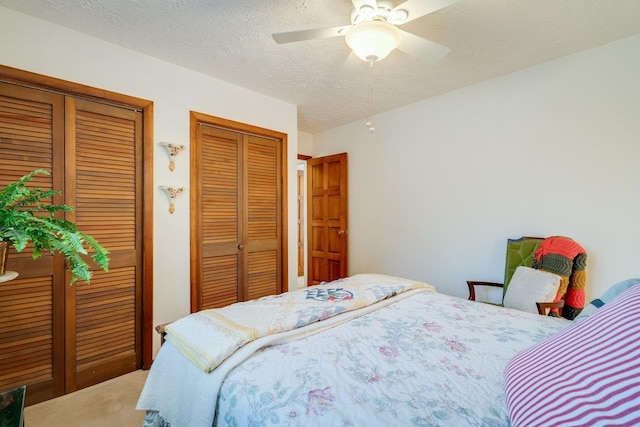 bedroom featuring ceiling fan, a textured ceiling, carpet, and multiple closets