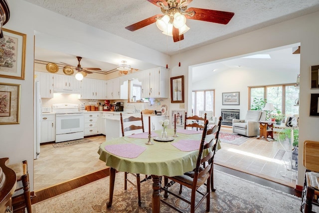 dining space with vaulted ceiling, a textured ceiling, a ceiling fan, and a glass covered fireplace