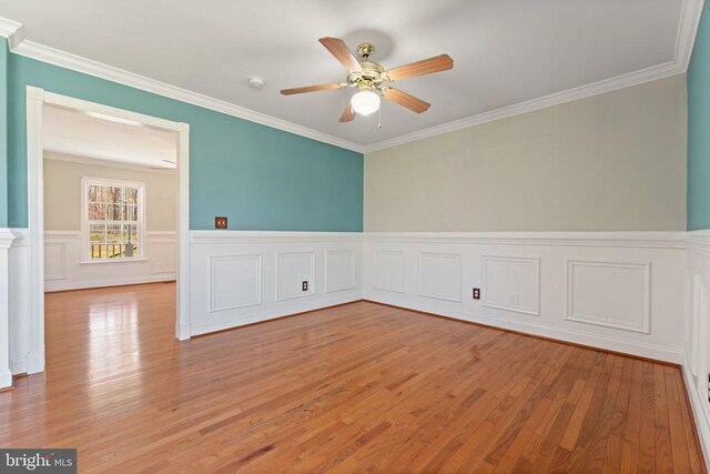spare room featuring a ceiling fan, light wood-style floors, ornamental molding, a wainscoted wall, and a smoke detector