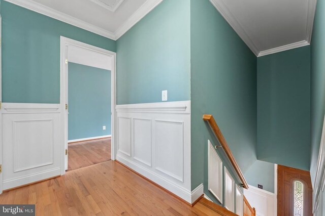 stairway with ornamental molding, wood finished floors, wainscoting, and a decorative wall