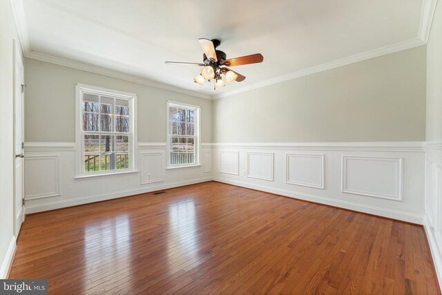 unfurnished room featuring a ceiling fan, a wainscoted wall, hardwood / wood-style flooring, and ornamental molding