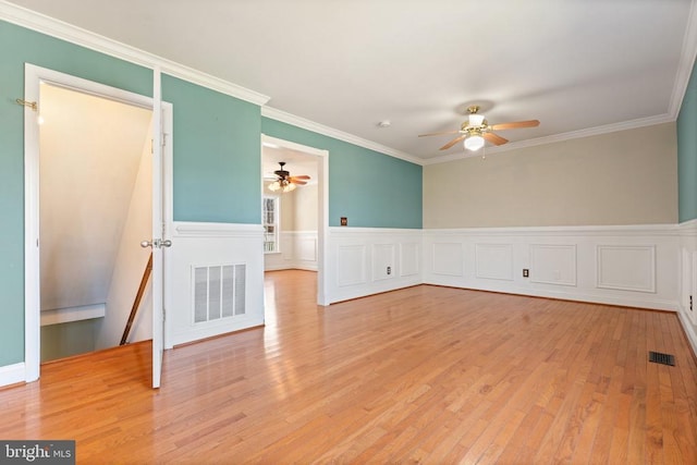 unfurnished room featuring ceiling fan, light wood-style floors, ornamental molding, and wainscoting