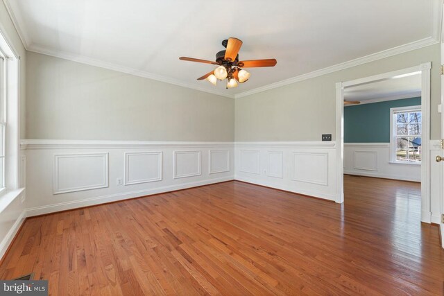 spare room featuring ceiling fan, wood finished floors, wainscoting, ornamental molding, and a decorative wall