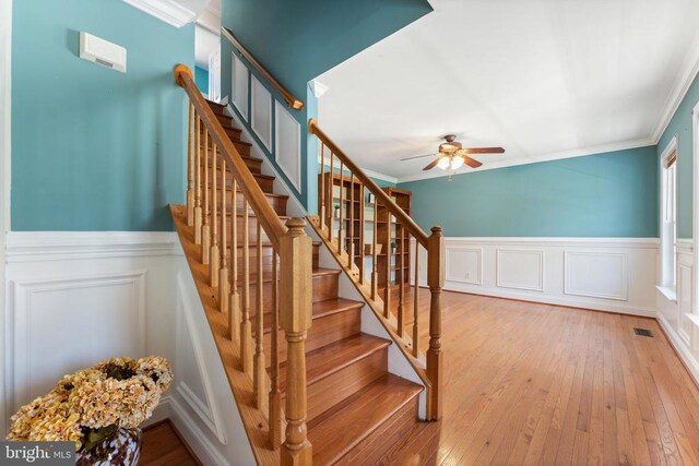 stairway featuring wainscoting, ceiling fan, ornamental molding, and wood-type flooring