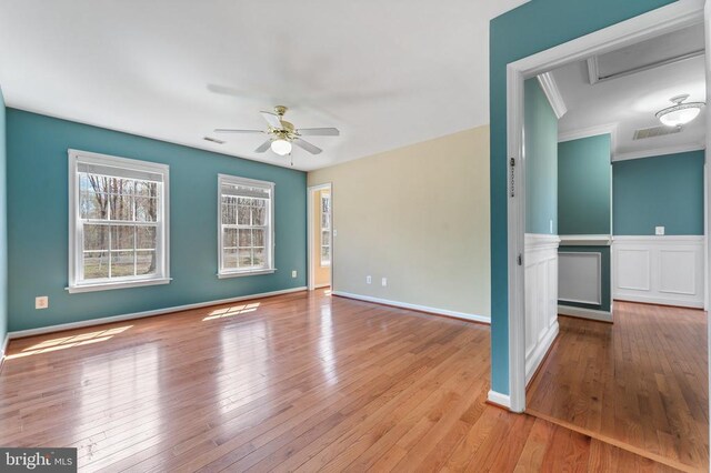 empty room with a ceiling fan, wood-type flooring, crown molding, and baseboards