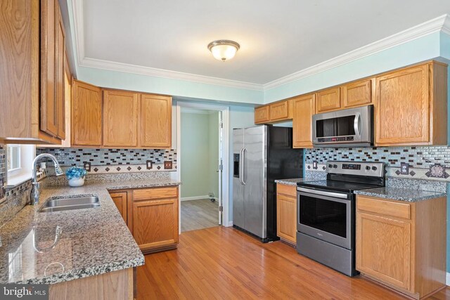 kitchen with stainless steel appliances, a sink, backsplash, light stone counters, and crown molding