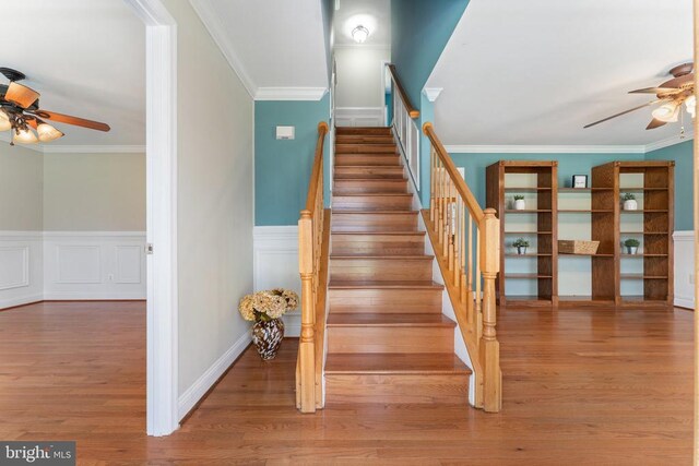 stairs featuring ceiling fan, wainscoting, wood finished floors, and ornamental molding