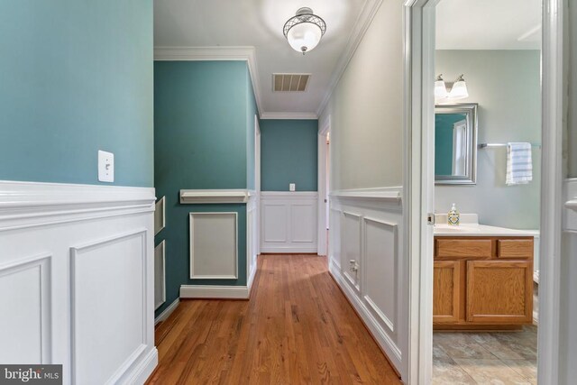 hallway with crown molding, a decorative wall, wainscoting, and wood finished floors