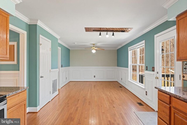 unfurnished dining area featuring light wood-type flooring, a ceiling fan, wainscoting, and ornamental molding