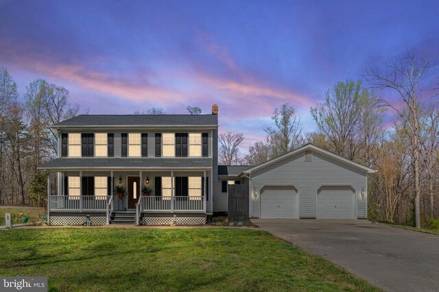 colonial-style house with covered porch, a garage, driveway, a chimney, and a lawn