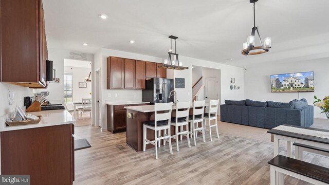kitchen with stainless steel refrigerator with ice dispenser, open floor plan, a breakfast bar, light countertops, and light wood-style floors