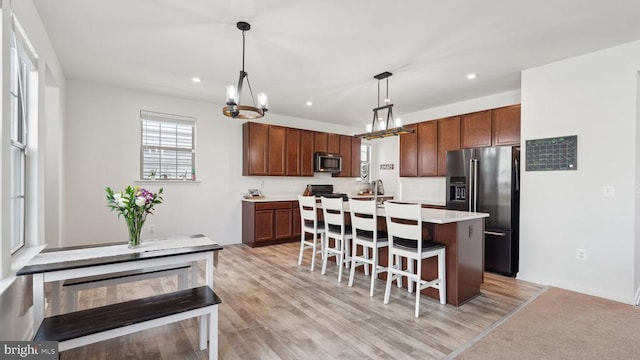 kitchen featuring stainless steel appliances, light countertops, a kitchen bar, a kitchen island, and decorative light fixtures
