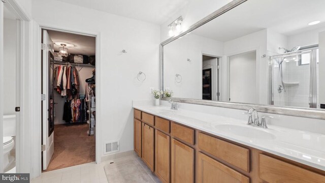 bathroom featuring toilet, a shower stall, double vanity, a walk in closet, and tile patterned floors