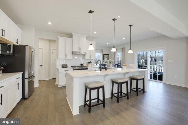 kitchen featuring stainless steel microwave, a kitchen breakfast bar, wood finished floors, backsplash, and a center island with sink