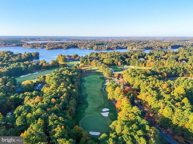drone / aerial view with view of golf course, a water view, and a view of trees