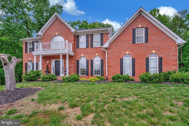 colonial house featuring a balcony, brick siding, and a front lawn