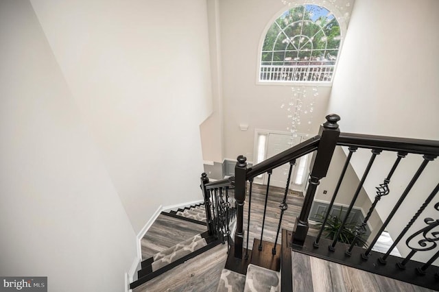 stairway with wood finished floors and a towering ceiling