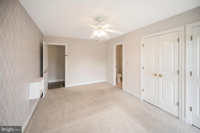 unfurnished bedroom featuring baseboards, light carpet, wallpapered walls, ensuite bath, and ceiling fan