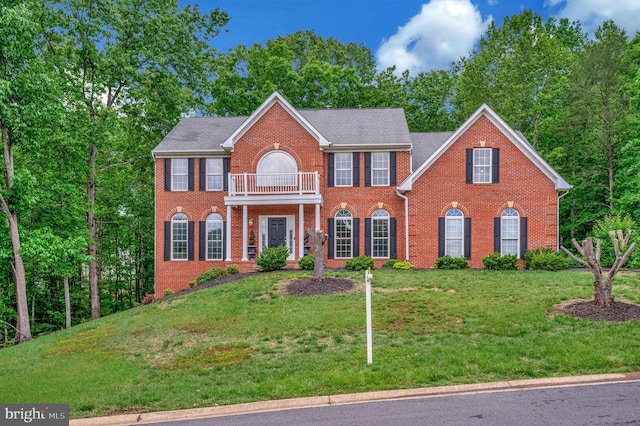 georgian-style home featuring a balcony, brick siding, and a front lawn
