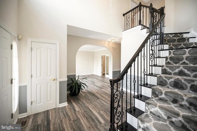 staircase featuring a towering ceiling, arched walkways, wood finished floors, and baseboards