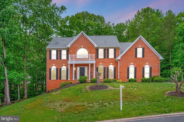 colonial house featuring a balcony, brick siding, and a front yard