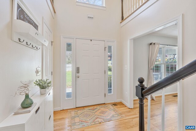 foyer entrance with a towering ceiling, light wood-style flooring, and baseboards