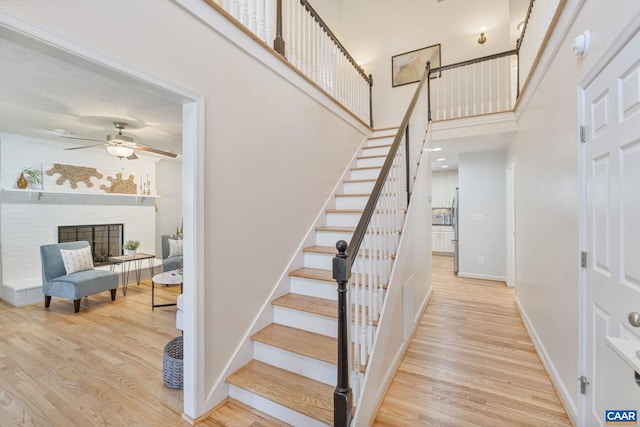 stairway with a high ceiling, wood finished floors, baseboards, and ceiling fan