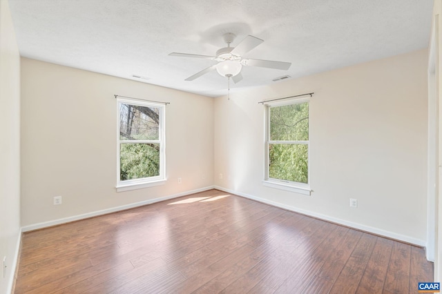 spare room with a ceiling fan, hardwood / wood-style floors, a healthy amount of sunlight, and visible vents