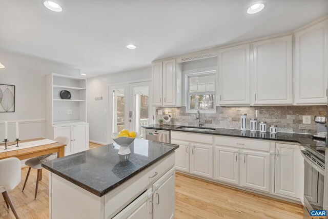 kitchen featuring appliances with stainless steel finishes, a sink, dark stone countertops, backsplash, and light wood-type flooring