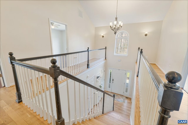 stairway featuring ceiling fan with notable chandelier, visible vents, high vaulted ceiling, and wood finished floors