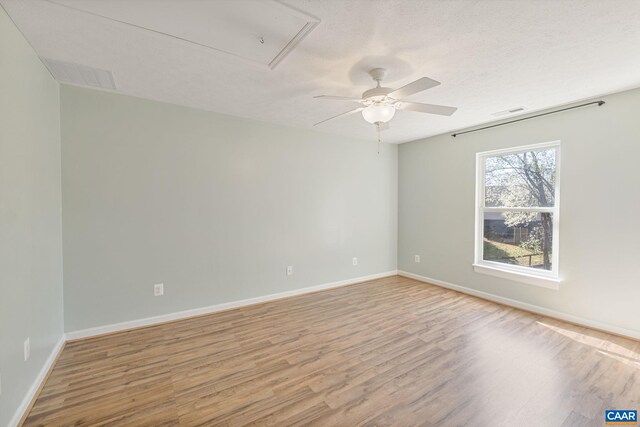empty room with wood finished floors, attic access, visible vents, ceiling fan, and baseboards