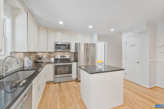 kitchen featuring light wood-style flooring, a center island, a sink, decorative backsplash, and stainless steel appliances